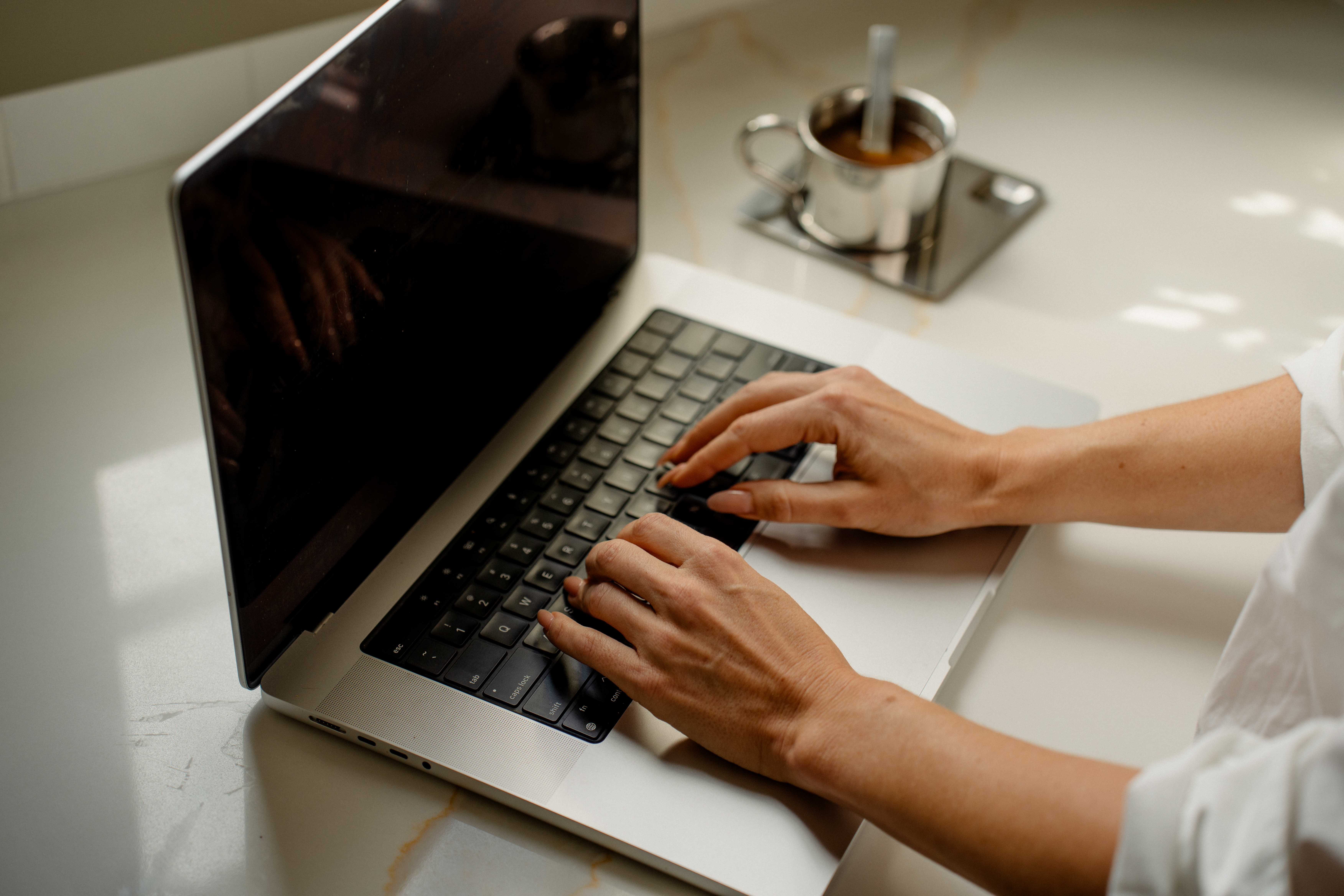 Hands typing on a laptop beside a cup of espresso